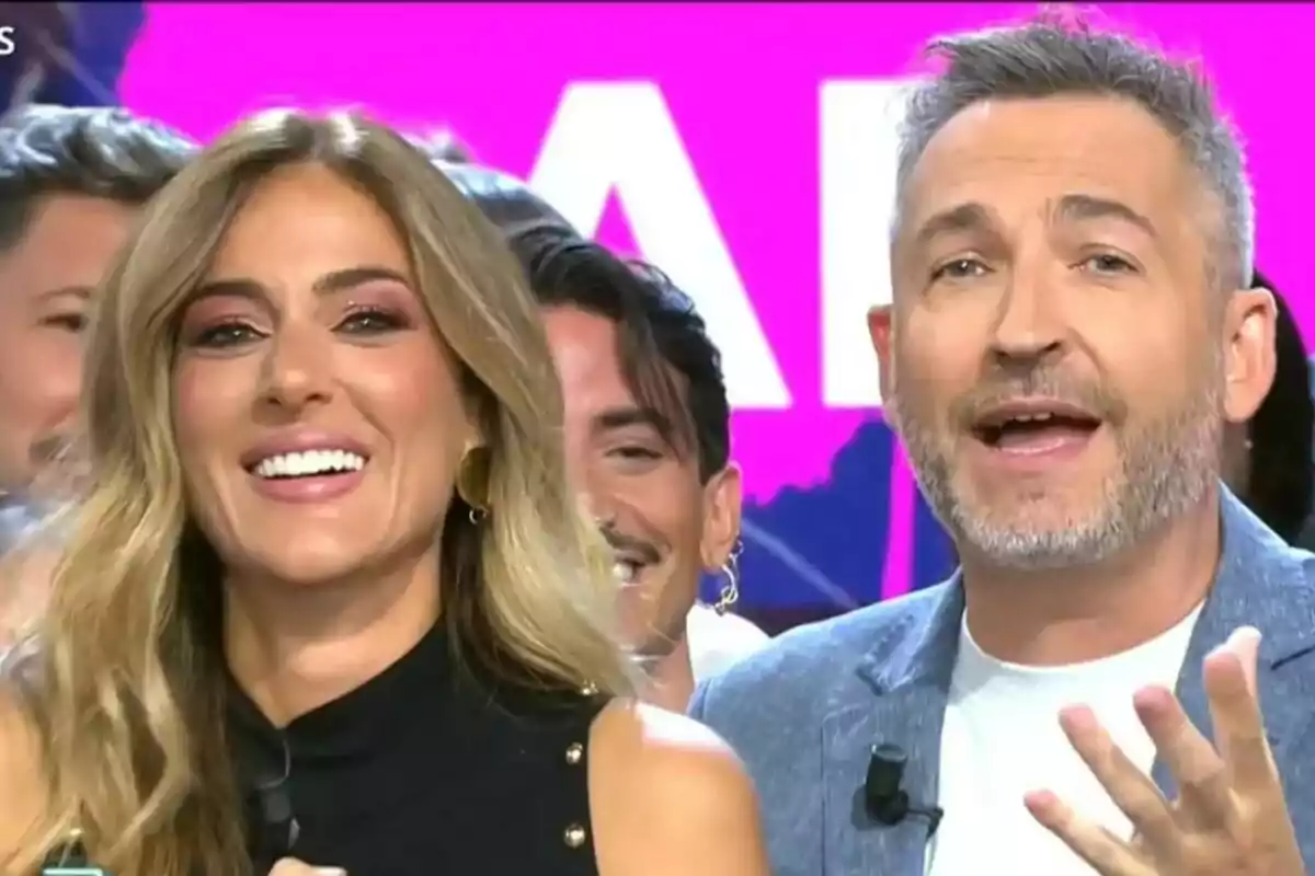 Verónica Dulanto i Frank Blanco somriuen i parlen a Tardear amb un fons acolorit i persones al darrere