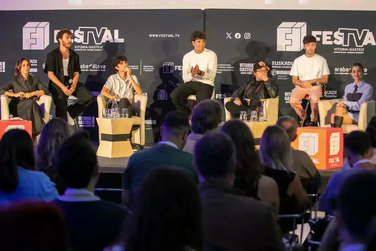 Un grupo de personas sentadas en sillones sobre un escenario participa en una charla sobre la serie Zoomers frente a una audiencia en un evento llamado FesTVal en Vitoria-Gasteiz