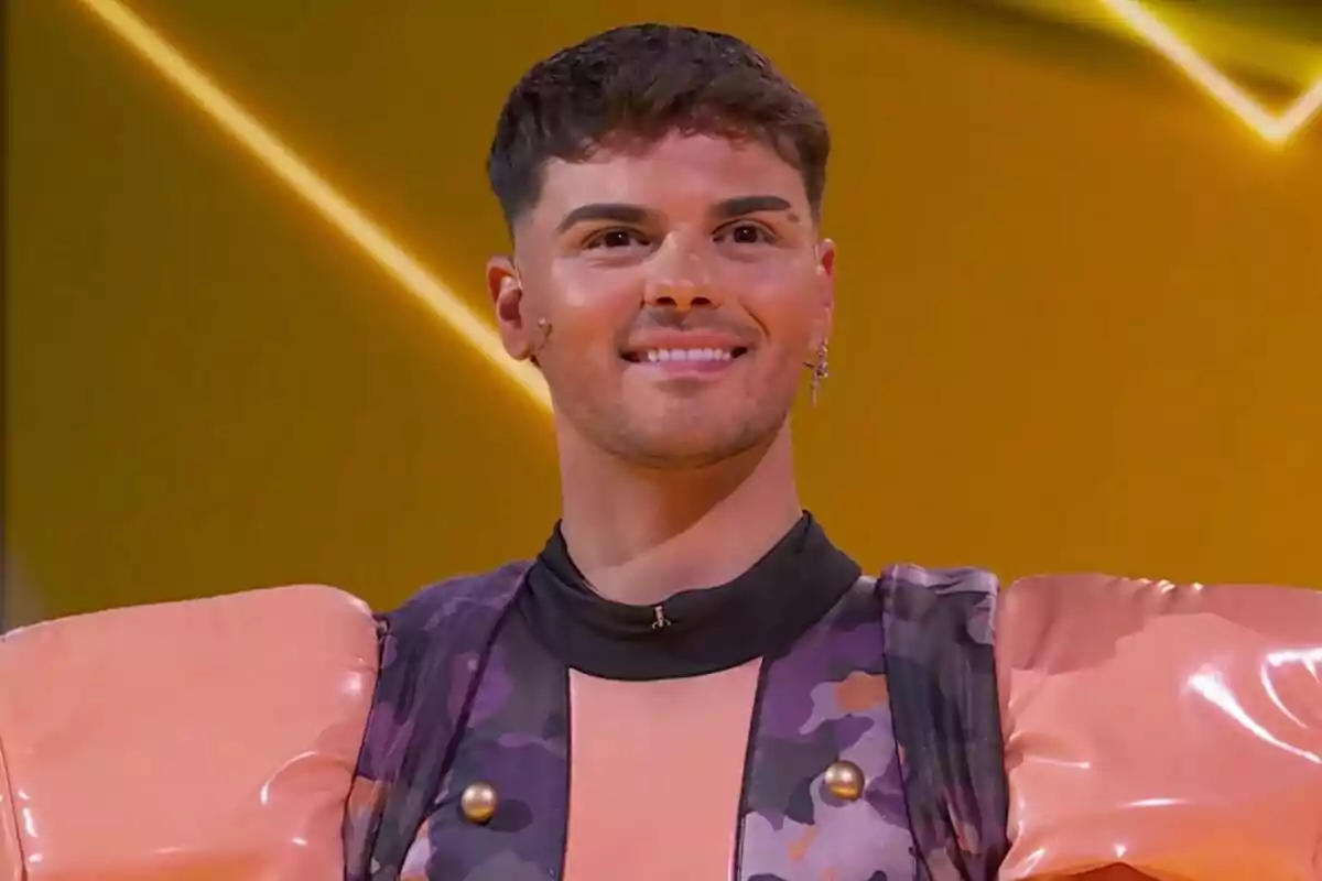 Abraham Mateo somrient amb un vestit colorit i muscleres grans en un fons groc a Mask Singer. Abraham Mateo somrient amb un vestit colorit i muscleres grans en un fons groc a Mask Singer.
