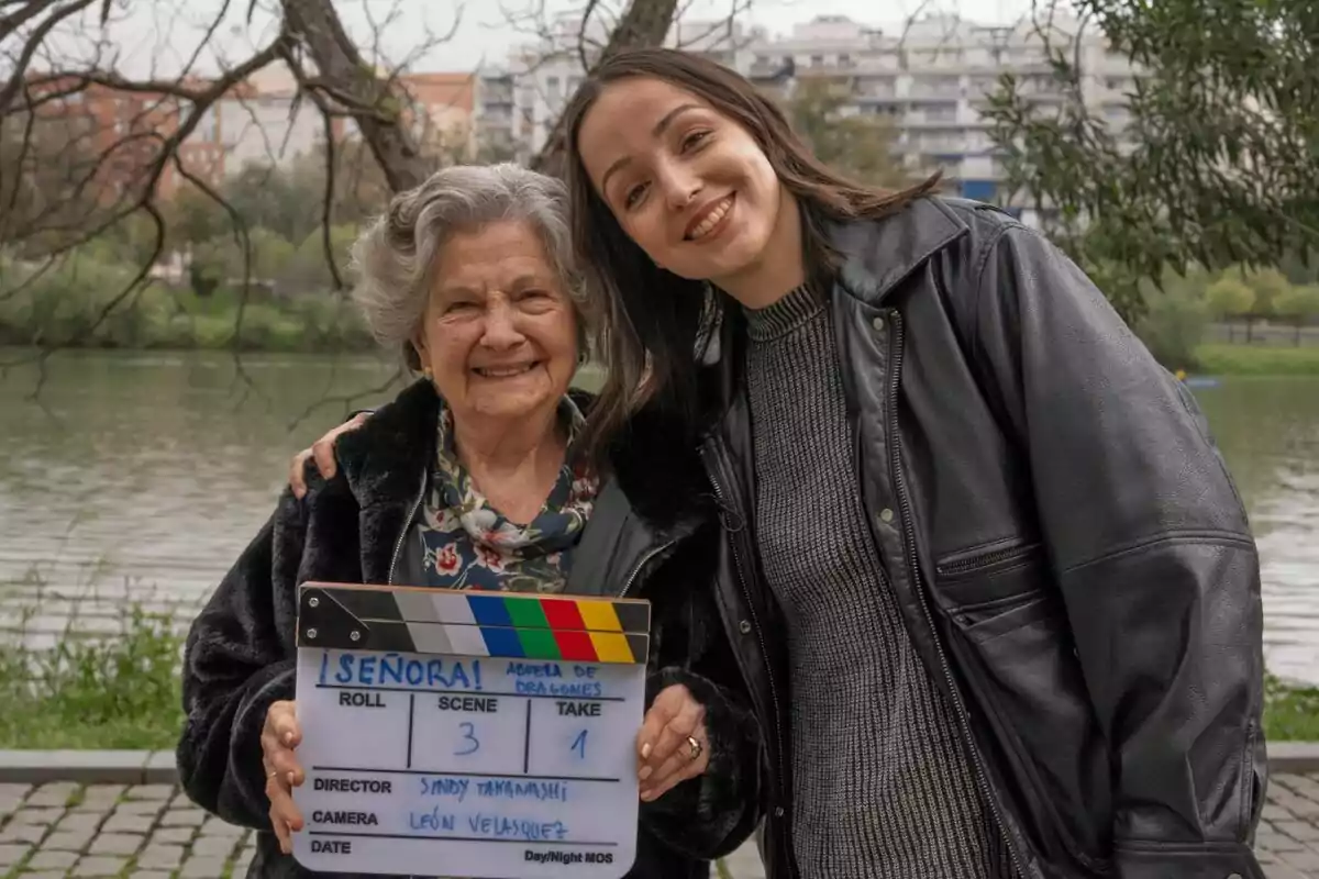 Abuela de dragones y Sindy Takanashi sonríen juntas al aire libre mientras sostienen una claqueta de cine de ¡Señora!.