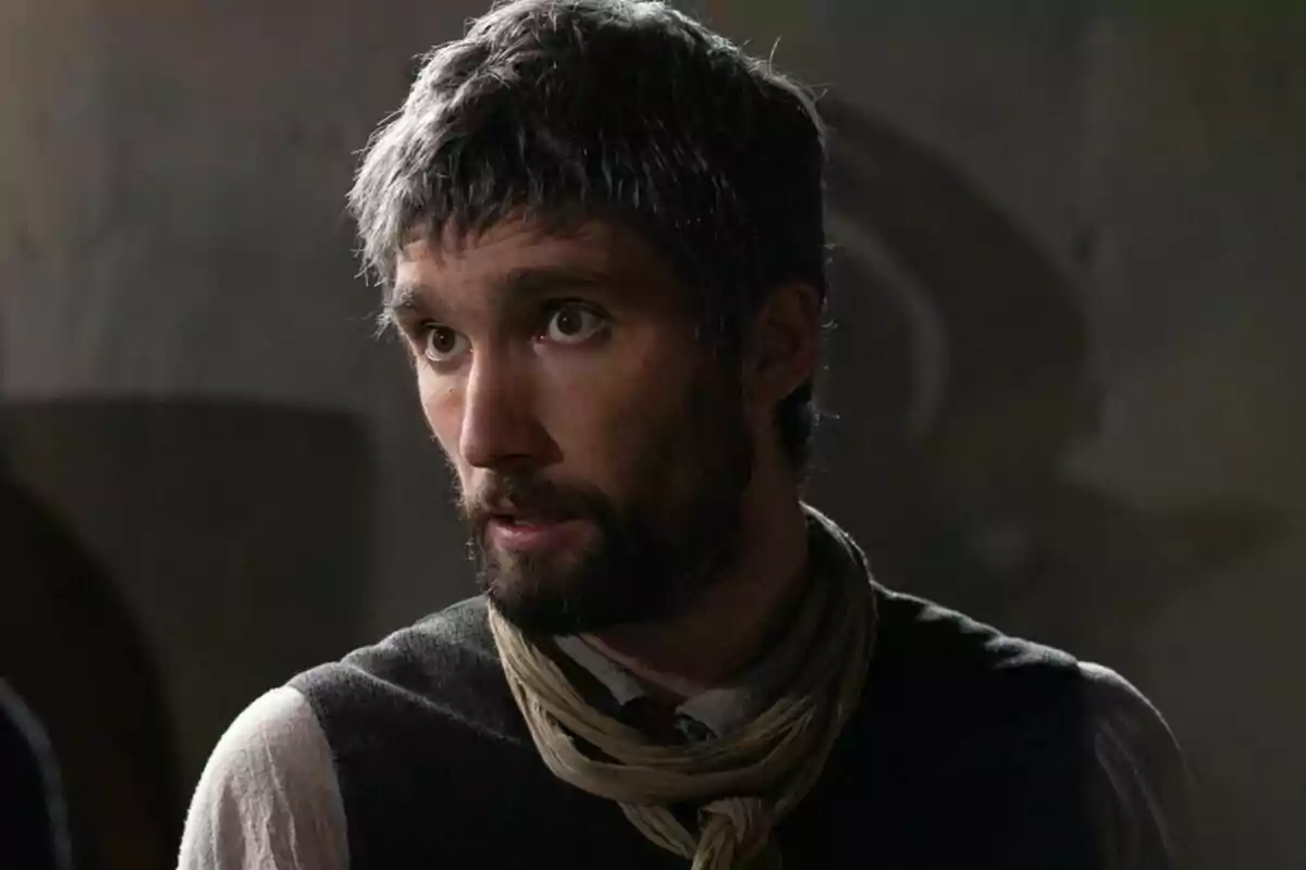 Chechu Salgado con barba y cabello oscuro, vistiendo un chaleco y una bufanda, mira hacia un lado con expresión seria en un ambiente con poca luz. Chechu Salgado con barba y cabello oscuro, vistiendo un chaleco y una bufanda, mira hacia un lado con expresión seria en un ambiente con poca luz.