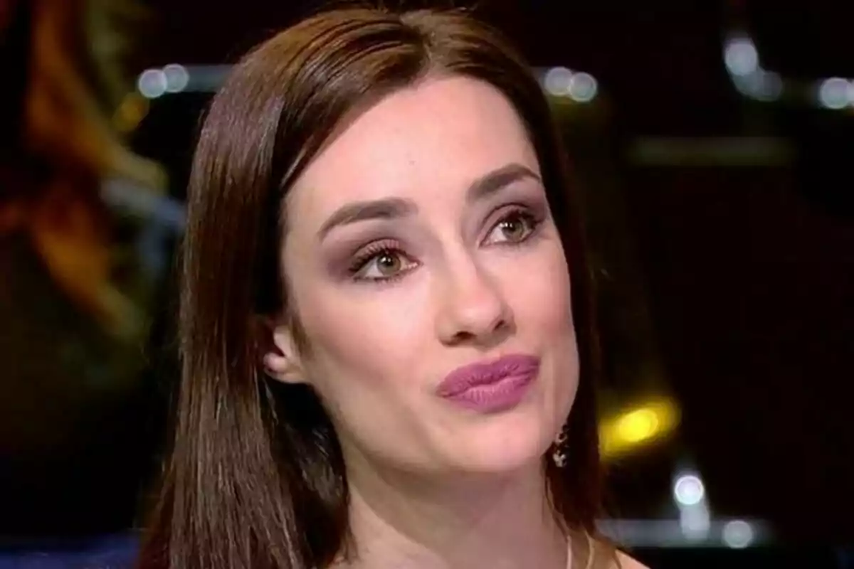 Adara Molinero con cabello castaño y expresión pensativa en un entorno oscuro.