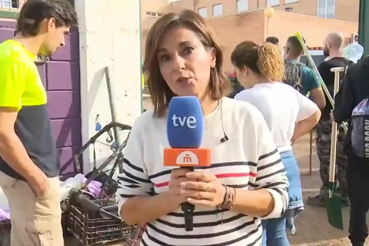 Adela González sostiene un micrófono de TVE de Mañaneros mientras está rodeada de personas y herramientas de limpieza en un entorno urbano. Adela González sostiene un micrófono de TVE de Mañaneros mientras está rodeada de personas y herramientas de limpieza en un entorno urbano.