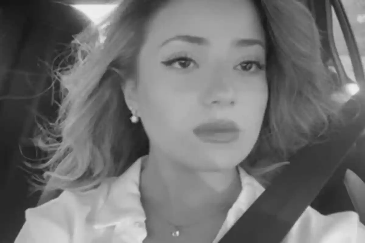 Fotografía en blanco y negro de Adriana Isabel Mojica con cabello suelto y expresión seria, usando cinturón de seguridad en un automóvil.