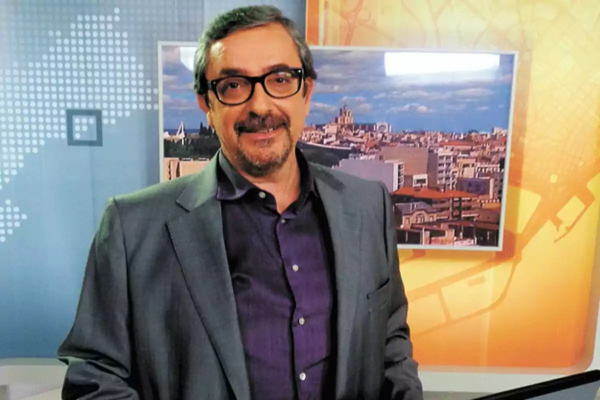 Agustí Forné amb ulleres i barba a un estudi de televisió amb fons de ciutat. Agustí Forné amb ulleres i barba a un estudi de televisió amb fons de ciutat.