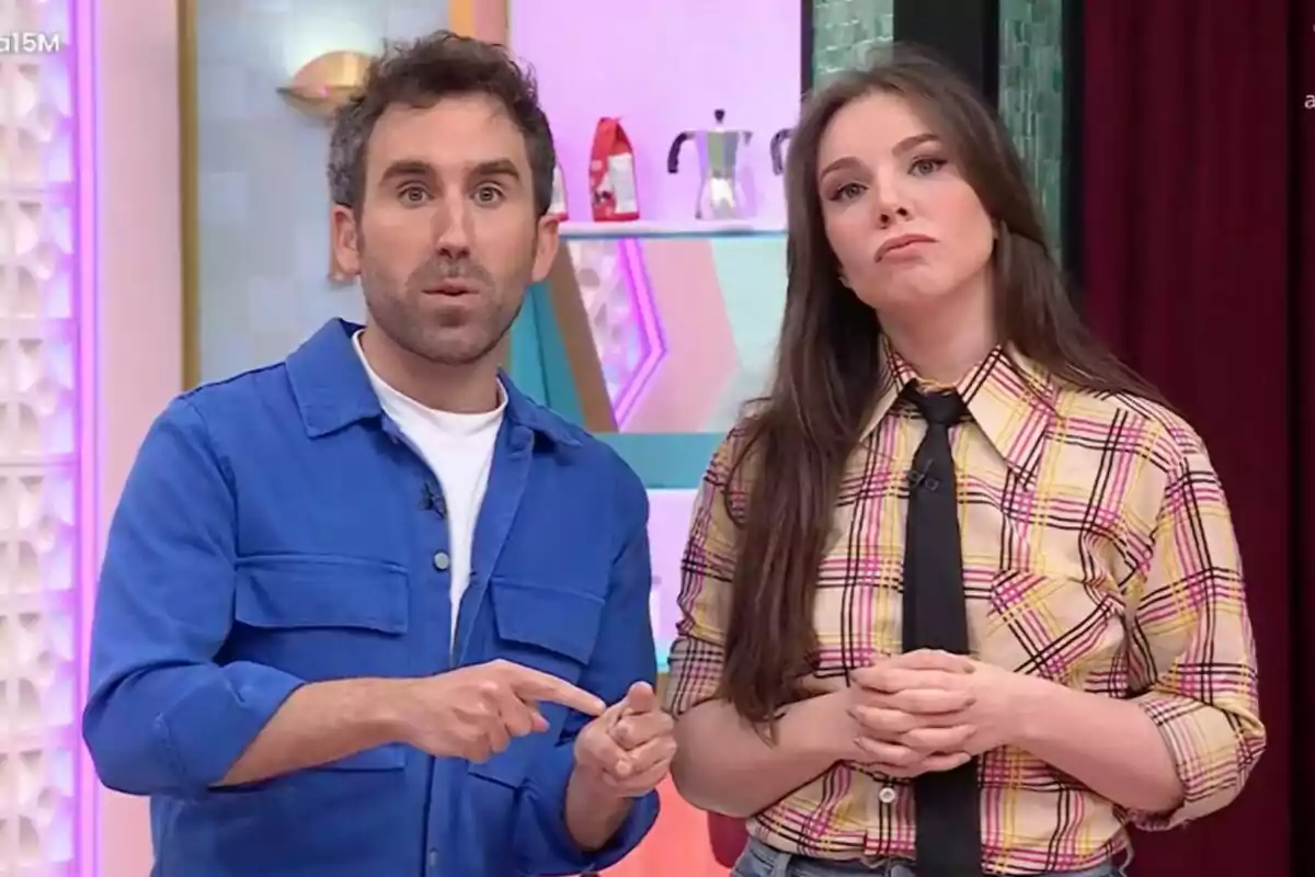 Aitor Albizua i Inés Hernand estan drets a La Família de la Tele, una d'elles porta una camisa blava i l'altra una camisa de quadres amb corbata negra.