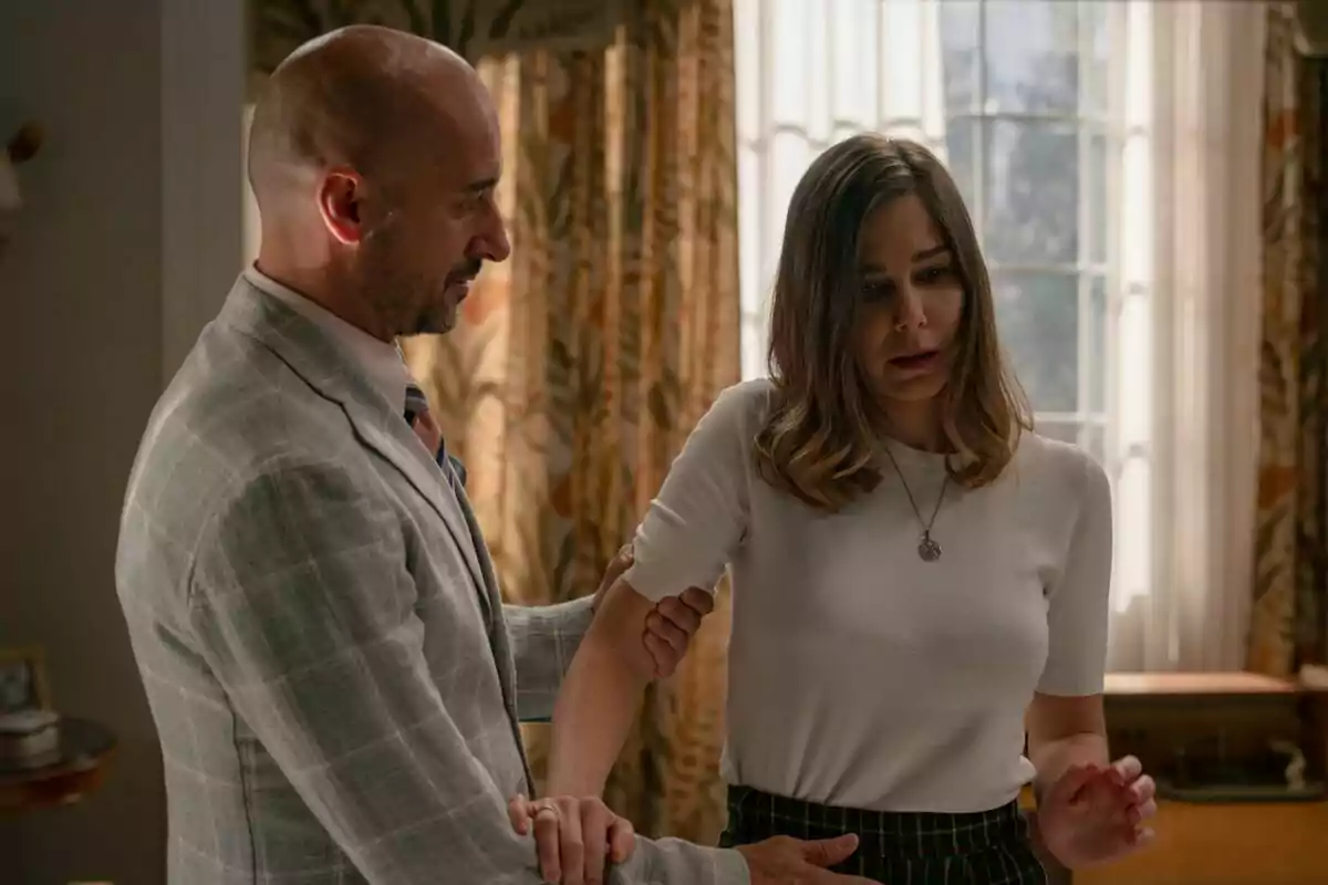 Alain Hernández con traje claro sostiene el brazo de Natalia Sánchez con expresión preocupada en una habitación con cortinas y luz natural en Sueños de Libertad Alain Hernández con traje claro sostiene el brazo de Natalia Sánchez con expresión preocupada en una habitación con cortinas y luz natural en Sueños de Libertad