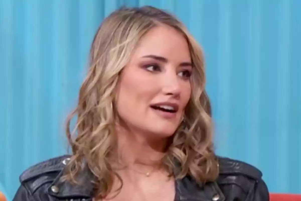 Alba Carrillo con cabello rubio y rizado lleva una chaqueta de cuero negra y está hablando frente a un fondo azul en Mañaneros.