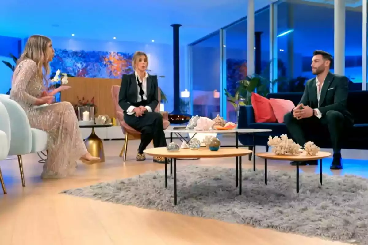 Alba, Gerad y Sandra Barneda sentadas en una sala moderna con decoración elegante y luces azules, conversando alrededor de mesas de centro con adornos en La Isla de las Tentaciones. Alba, Gerad y Sandra Barneda sentadas en una sala moderna con decoración elegante y luces azules, conversando alrededor de mesas de centro con adornos en La Isla de las Tentaciones.