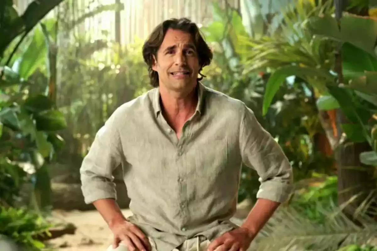 Álex Adrover con camisa de lino claro está sentado en un entorno tropical rodeado de plantas verdes en Supervivientes. Álex Adrover con camisa de lino claro está sentado en un entorno tropical rodeado de plantas verdes en Supervivientes.