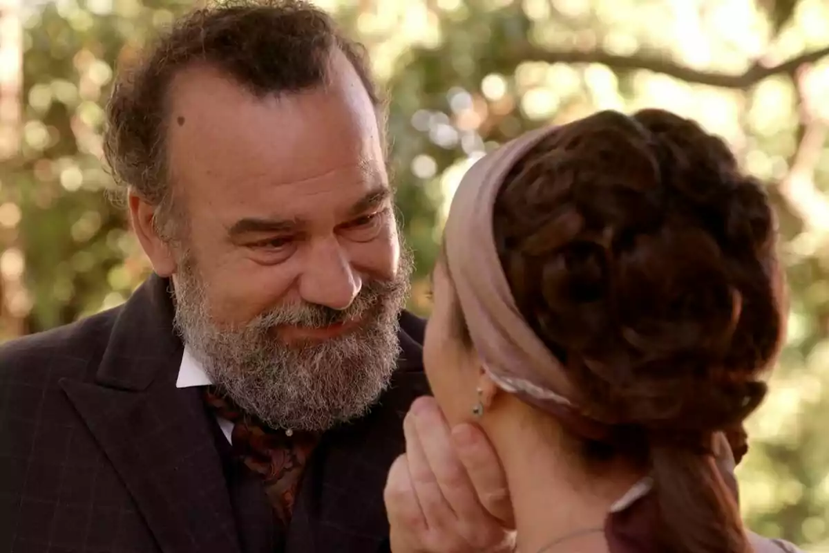 Manuel Regueiro amb barba somriu mentre sosté la cara de Carmen Asecas amb un mocador als cabells en un entorn a l'aire lliure a La Promesa. Manuel Regueiro amb barba somriu mentre sosté la cara de Carmen Asecas amb un mocador als cabells en un entorn a l'aire lliure a La Promesa.