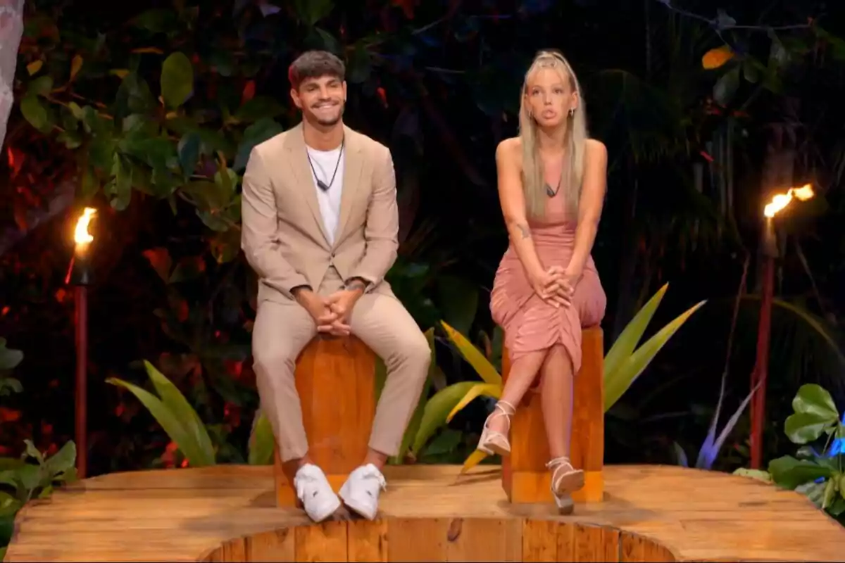 Álvaro y Alba sentadas en un escenario al aire libre rodeado de vegetación y antorchas, una de ellas lleva un traje beige y la otra un vestido rosa en La Isla de las Tentaciones. Álvaro y Alba sentadas en un escenario al aire libre rodeado de vegetación y antorchas, una de ellas lleva un traje beige y la otra un vestido rosa en La Isla de las Tentaciones.