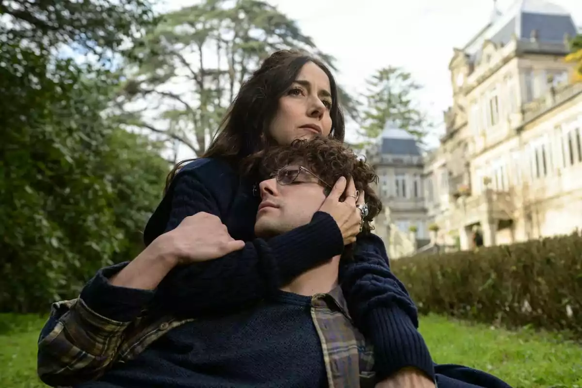 Cecilia Suárez abraza a Álvaro Rico mientras están sentados en un jardín con un edificio antiguo al fondo en El Jardinero.