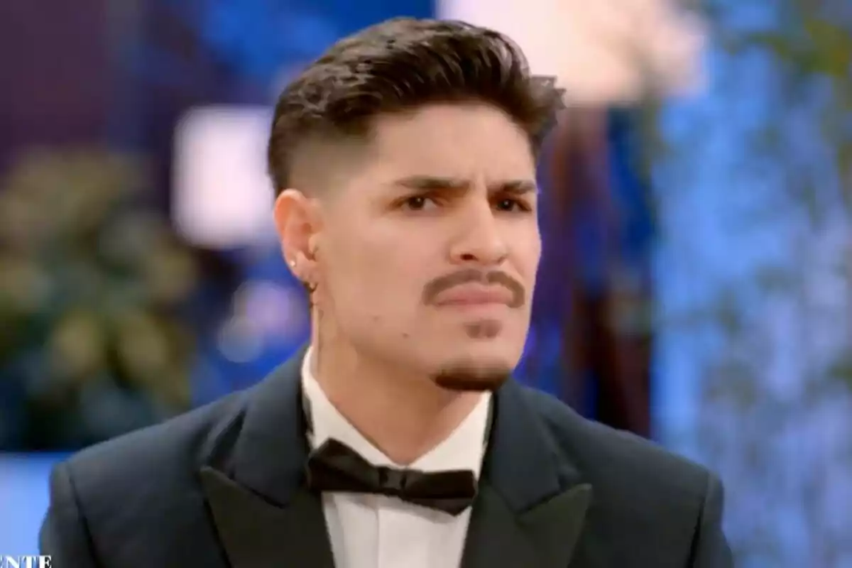 Álvaro con expresión de confusión o duda, vestido con un esmoquin y corbata de moño, en un entorno interior con luces difusas al fondo en La Isla de las Tentaciones. Álvaro con expresión de confusión o duda, vestido con un esmoquin y corbata de moño, en un entorno interior con luces difusas al fondo en La Isla de las Tentaciones.