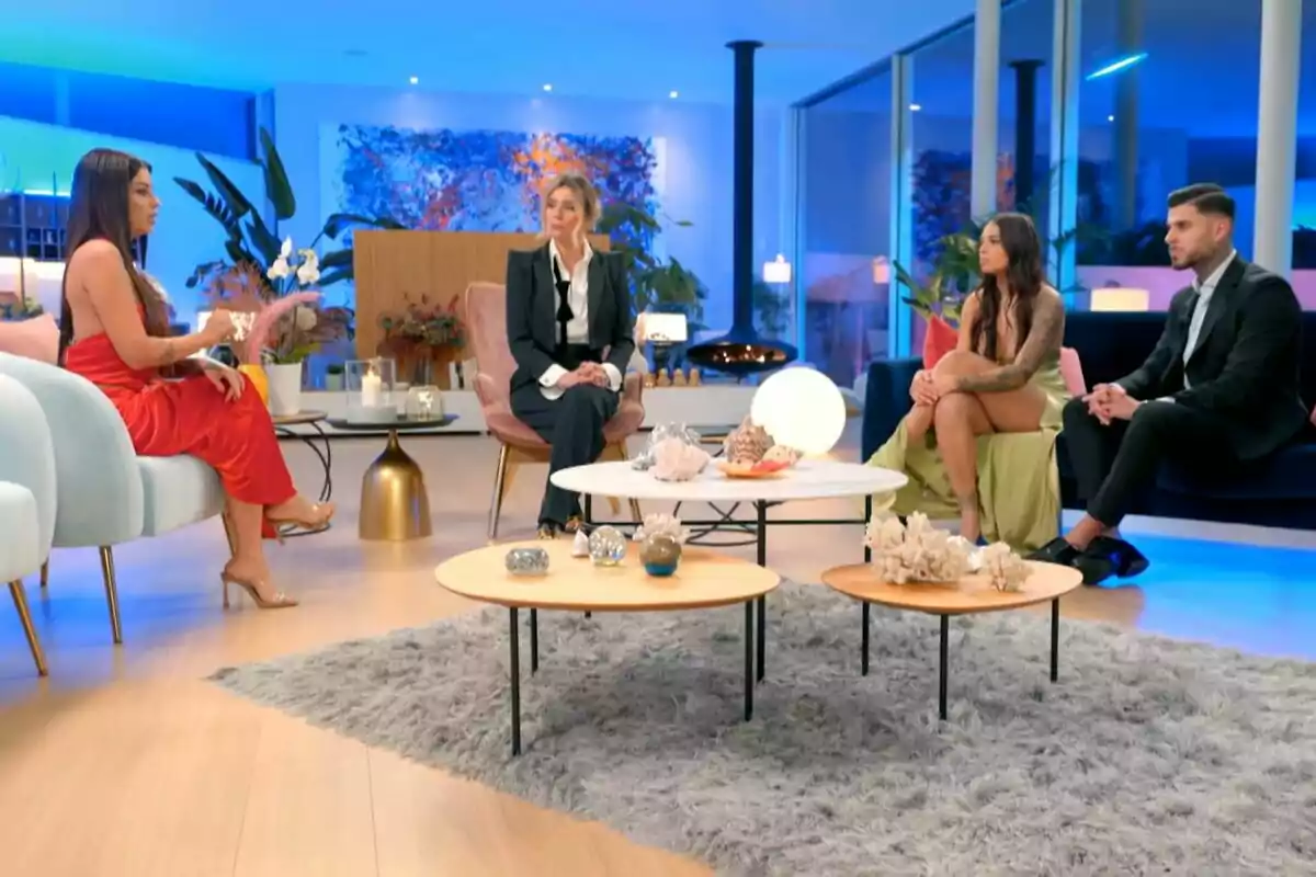 Un grupo de personas formado por Gabriella, Sandra Barneda, Ana y Fran sentadas en un salón moderno con decoración elegante y luz azul ambiental en La Isla de las Tentaciones. Un grupo de personas formado por Gabriella, Sandra Barneda, Ana y Fran sentadas en un salón moderno con decoración elegante y luz azul ambiental en La Isla de las Tentaciones.