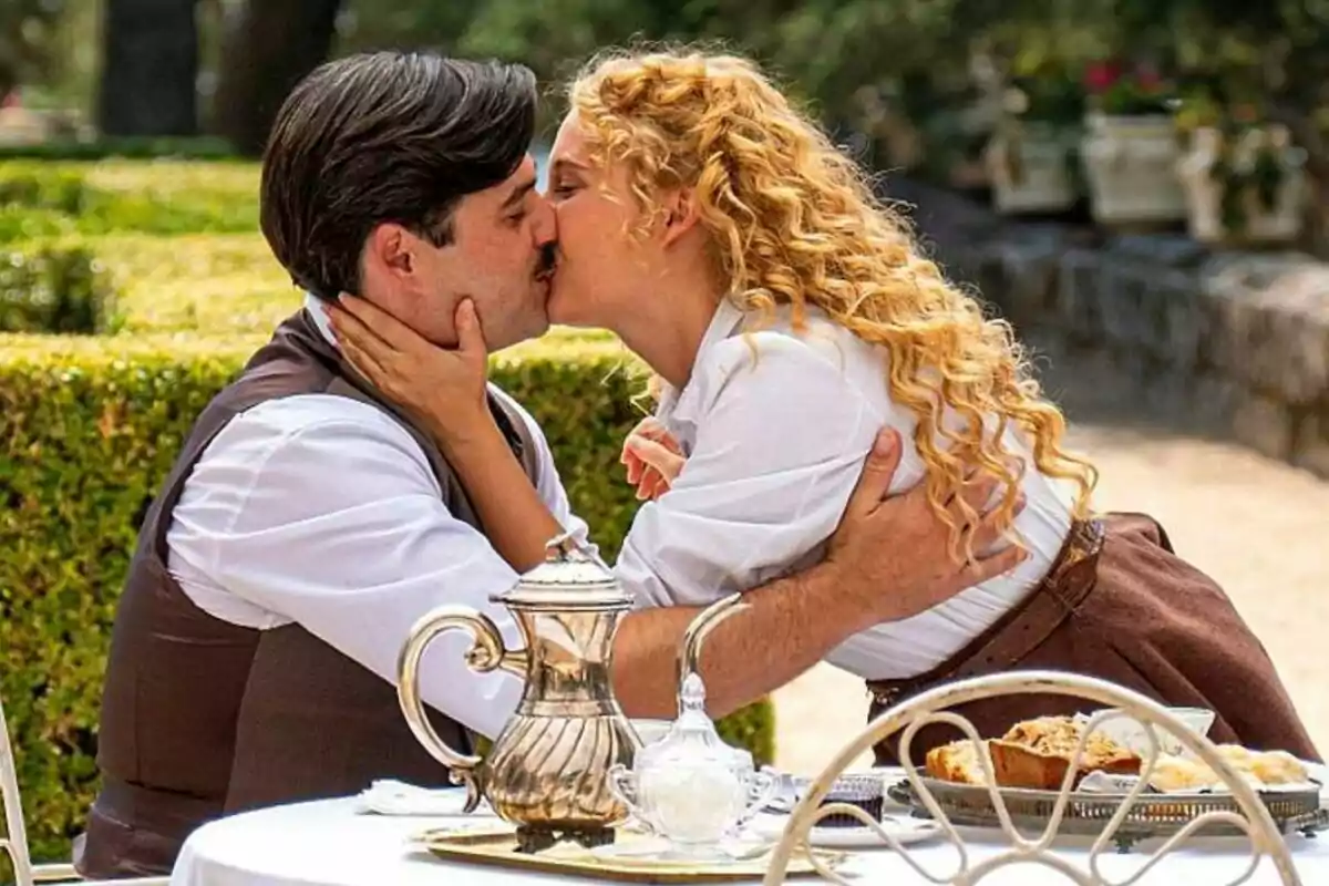 Arturo Sancho i Ana Garcés es besen apassionadament en un jardí mentre estan asseguts en una taula amb un servei de te a La Promesa. Arturo Sancho i Ana Garcés es besen apassionadament en un jardí mentre estan asseguts en una taula amb un servei de te a La Promesa.
