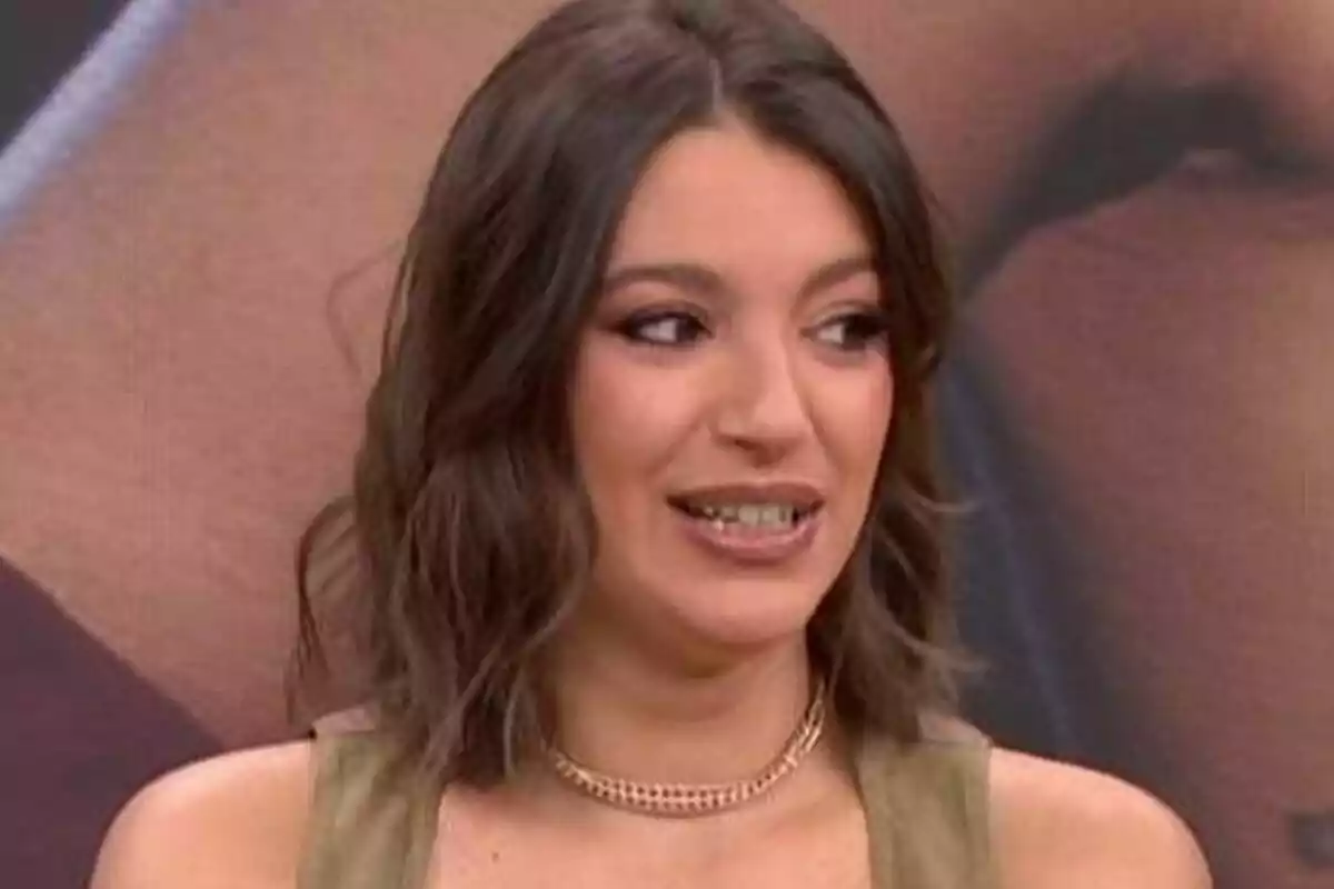 Ana Guerra con cabello castaño y maquillaje sutil sonríe mientras mira hacia un lado en Espejo Público.