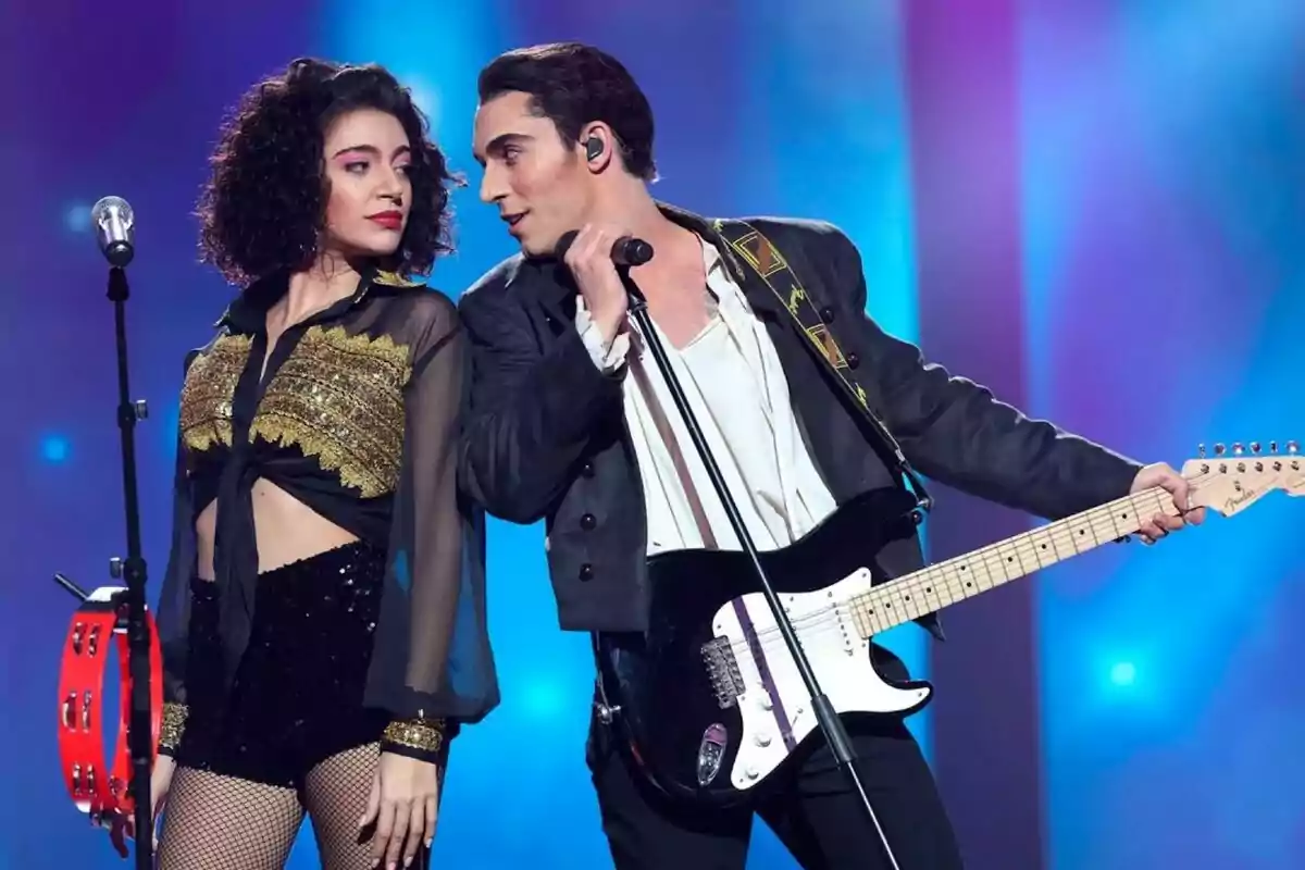 Ana Guerra i Víctor Elías a l'escenari, la dona sosté una pandereta i l'home una guitarra elèctrica, tots dos mirant-se mentre actuen sota llums de colors a Tu Cara Me Suena.