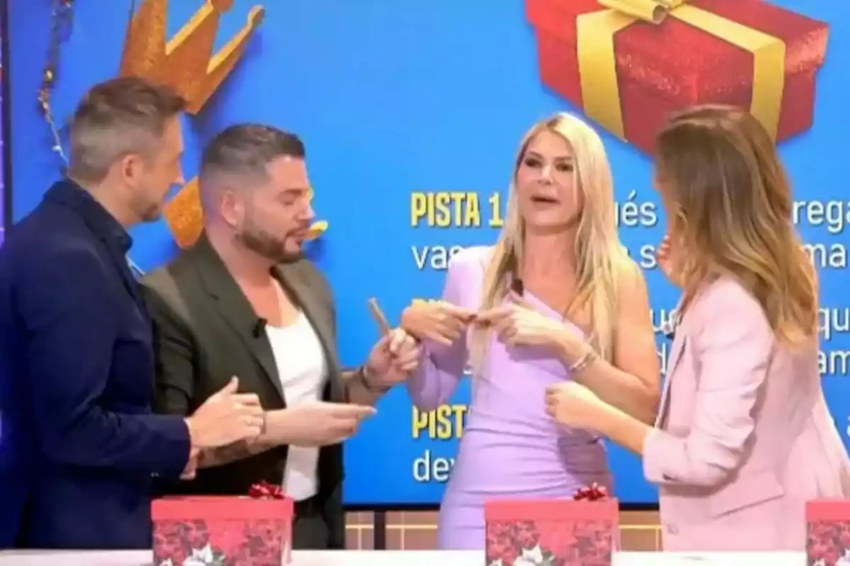 Verónica Dulanto, Frank Blanco, Ana Luque i Alberto Dugarte interactuen a Festa amb un fons blau i caixes de regal vermelles sobre una taula. Verónica Dulanto, Frank Blanco, Ana Luque i Alberto Dugarte interactuen a Festa amb un fons blau i caixes de regal vermelles sobre una taula.