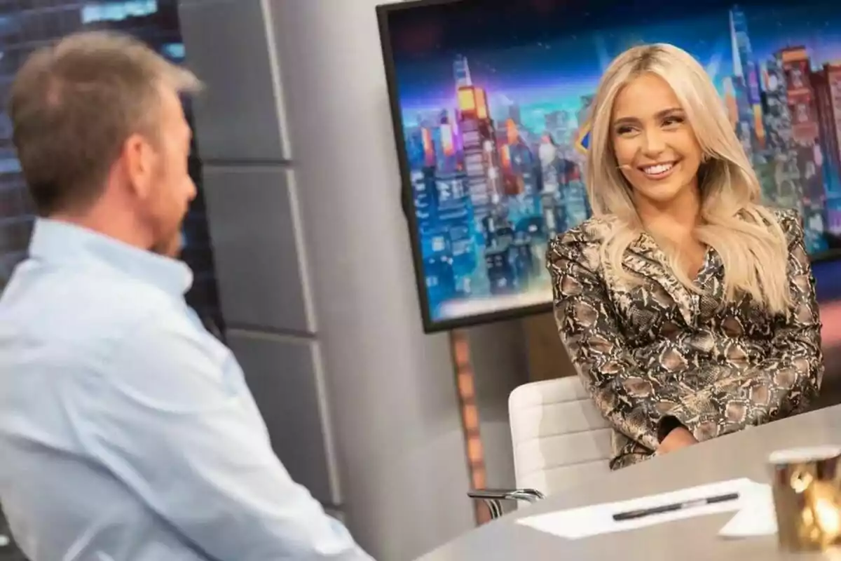 Ana Mena y Pablo Motos conversan en el plató de El Hormiguero, una mujer rubia sonríe mientras un hombre de cabello corto y barba la escucha atentamente. Ana Mena y Pablo Motos conversan en el plató de El Hormiguero, una mujer rubia sonríe mientras un hombre de cabello corto y barba la escucha atentamente.