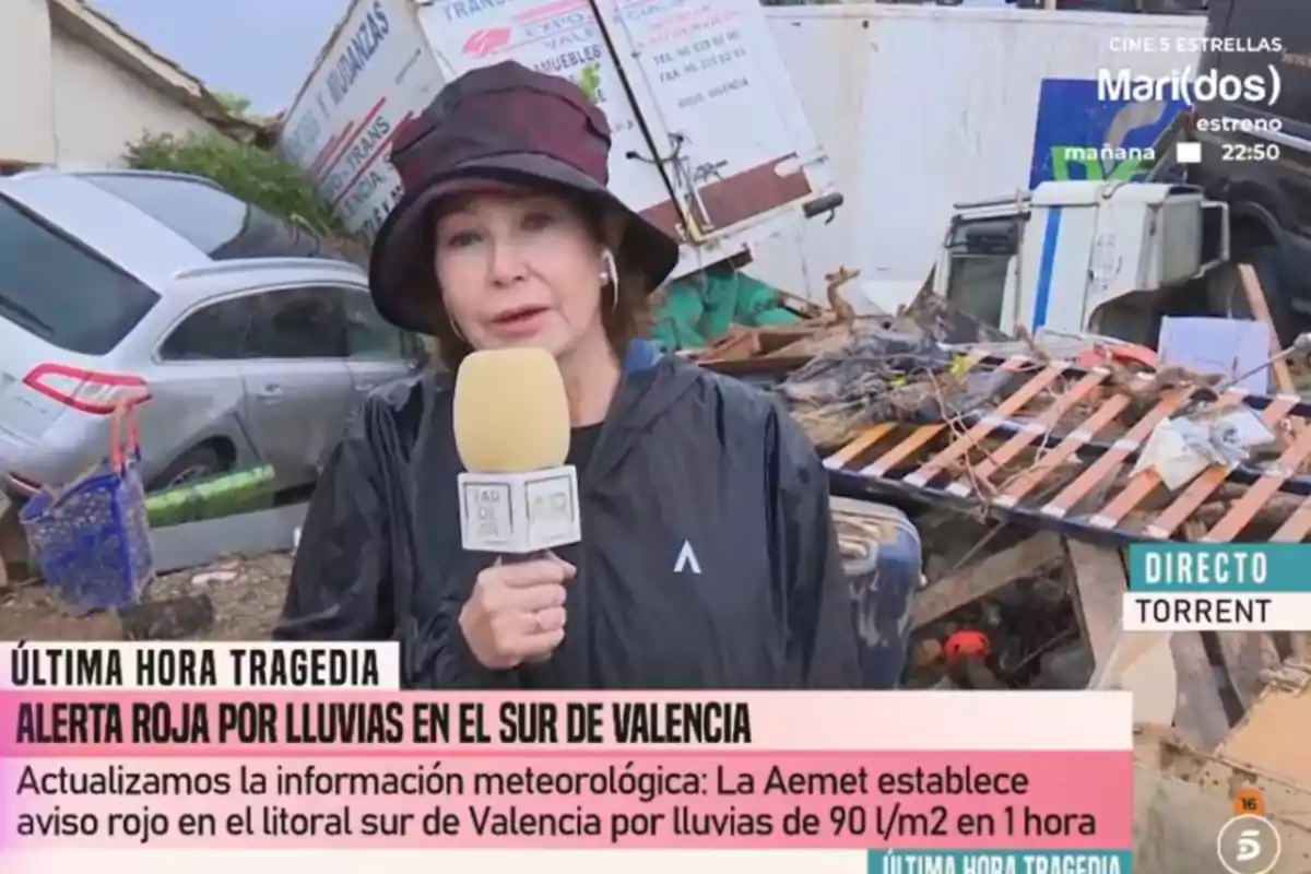 Ana Rosa Quintana informando sobre una alerta roja por lluvias en el sur de Valencia, con vehículos y escombros visibles en el fondo. Ana Rosa Quintana informando sobre una alerta roja por lluvias en el sur de Valencia, con vehículos y escombros visibles en el fondo.