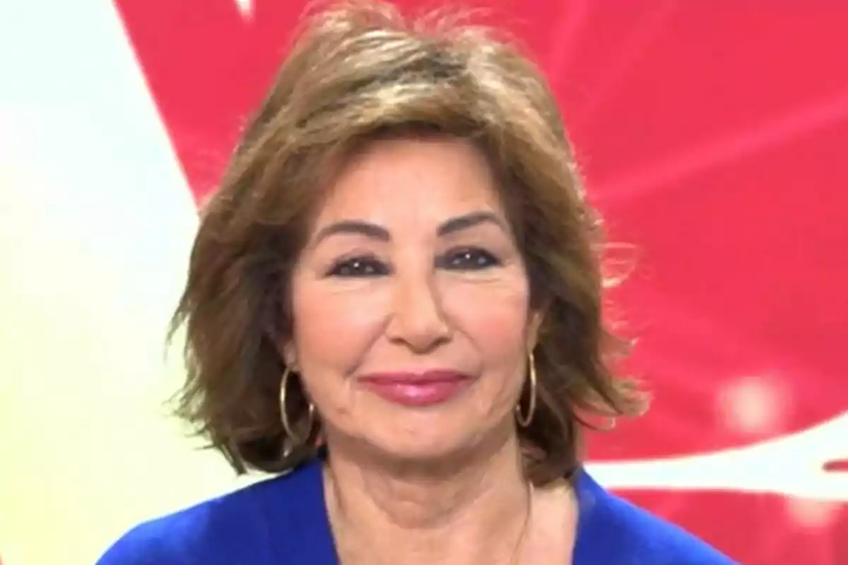 Ana Rosa Quintana amb cabell castany i arracades daurades somriu davant d'un fons vermell a El Programa de Ana Rosa.