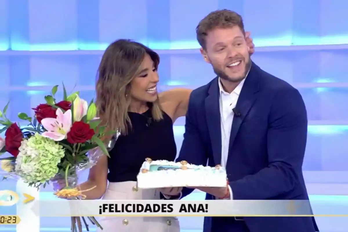 Ana Terradillos y Jano Mecha sostienen un pastel y un ramo de flores con un mensaje de felicitación en la parte inferior de la imagen en La Mirada Crítica. Ana Terradillos y Jano Mecha sostienen un pastel y un ramo de flores con un mensaje de felicitación en la parte inferior de la imagen en La Mirada Crítica.