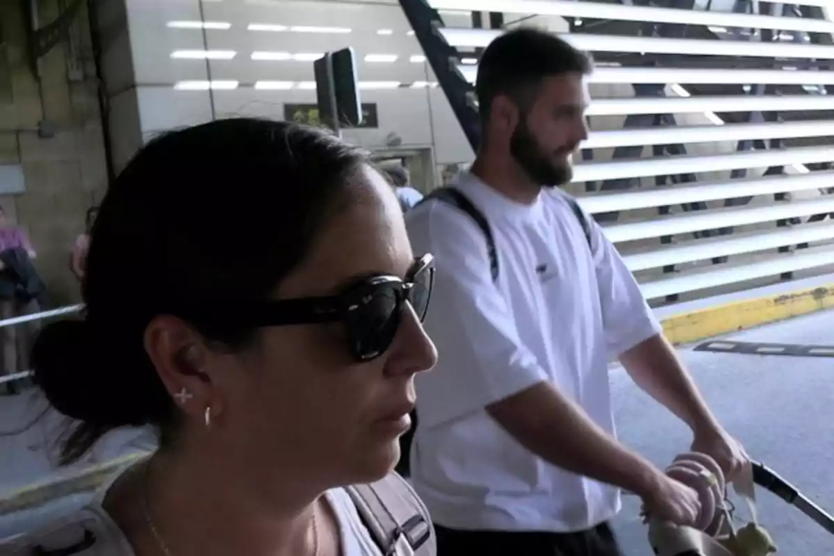 Anabel Pantoja amb ulleres de sol i David Rodríguez amb samarreta blanca empenyent un cotxet de nadó en un entorn urbà. Anabel Pantoja amb ulleres de sol i David Rodríguez amb samarreta blanca empenyent un cotxet de nadó en un entorn urbà.