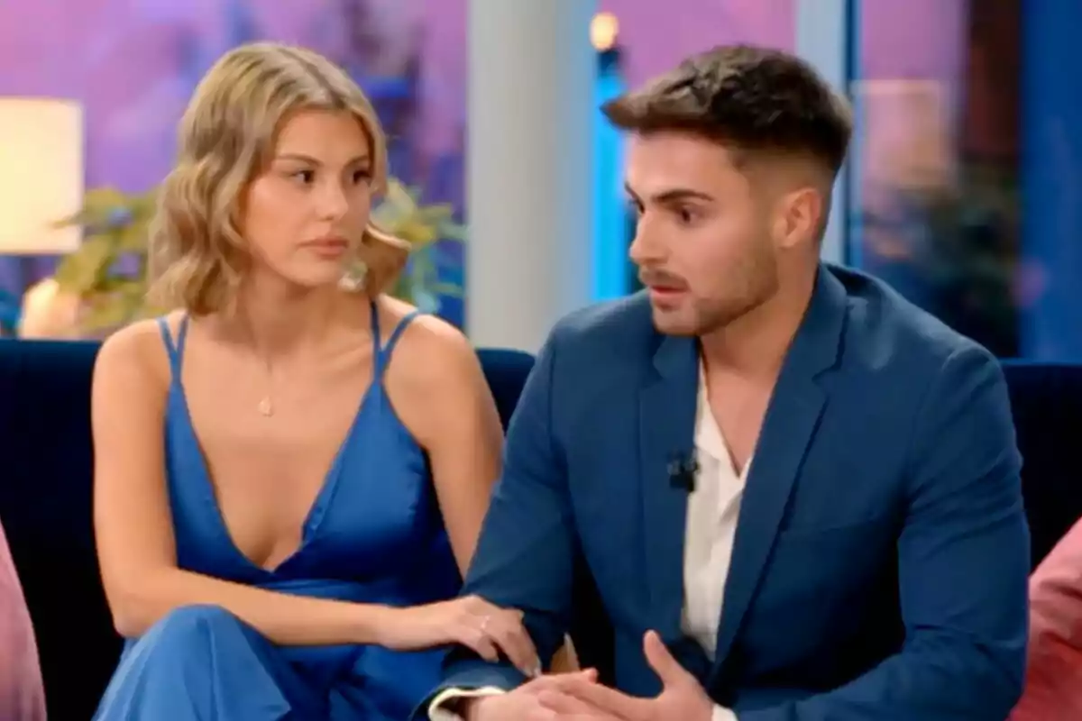 Andrea y Joel sentados en un sofá, ambos vestidos de azul, parecen estar en una conversación seria en La Isla de las Tentaciones.