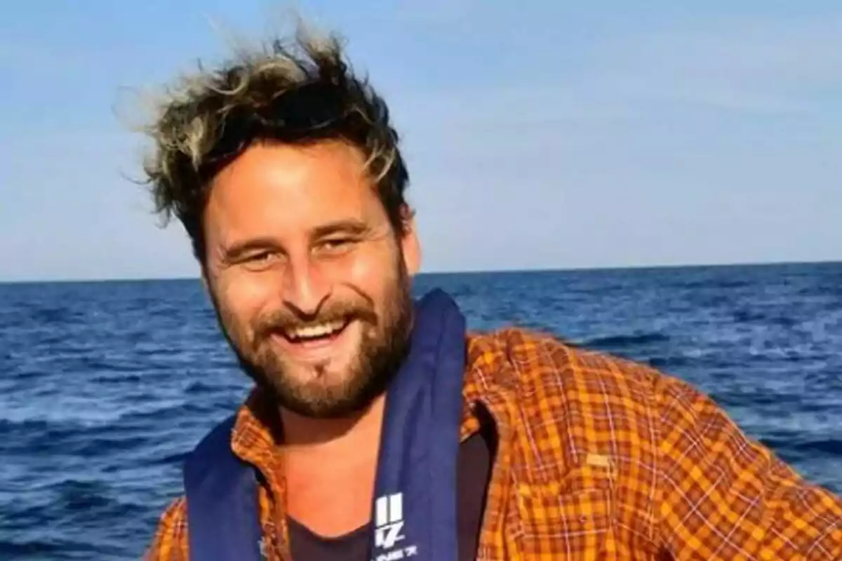 Fotografía de Andrew Jury con camisa a cuadros y chaleco salvavidas azul en un barco con el mar de fondo. Fotografía de Andrew Jury con camisa a cuadros y chaleco salvavidas azul en un barco con el mar de fondo.