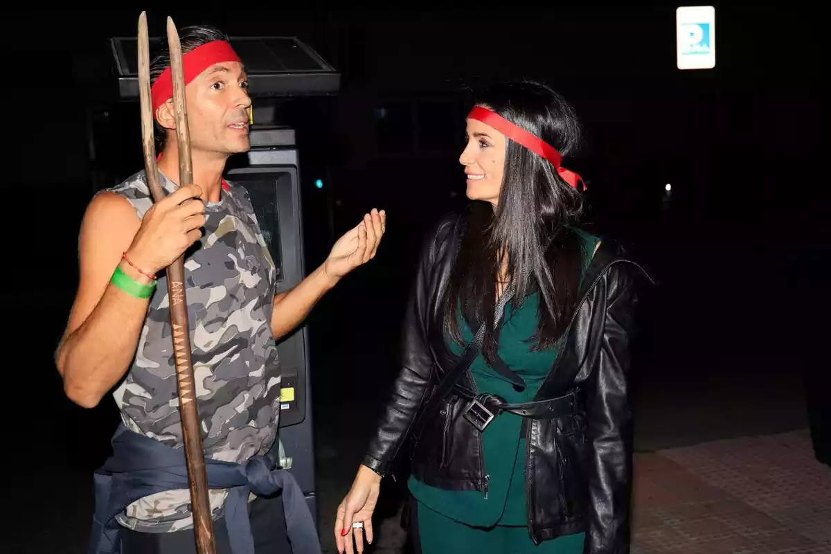 Ángel Cristo hablando con una cinta roja en la frente, una camiseta militar y un palo en la mano junto a Ana Herminia sonriendo con una cinta roja en la cabeza y una chaqueta negra Ángel Cristo hablando con una cinta roja en la frente, una camiseta militar y un palo en la mano junto a Ana Herminia sonriendo con una cinta roja en la cabeza y una chaqueta negra