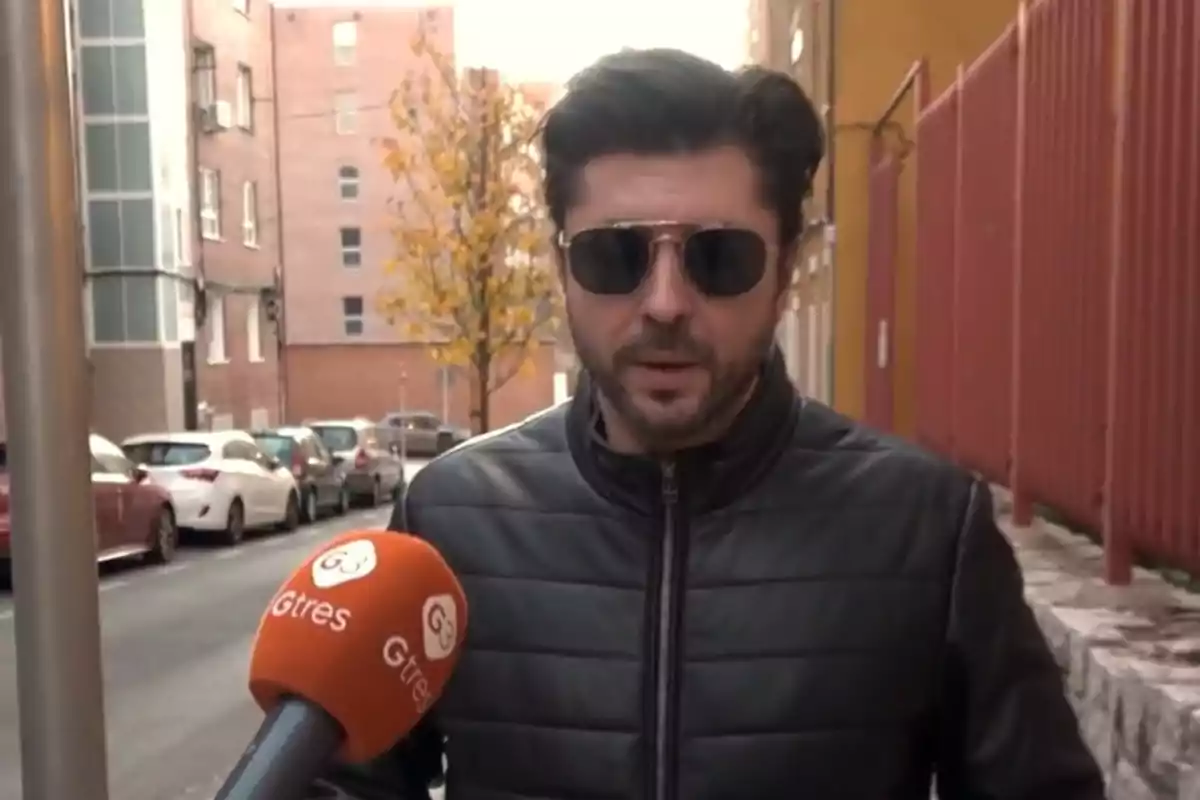 Ángel Cristo, con chaqueta negra y gafas de sol, es entrevistado en la calle por un micrófono naranja de Gtres Ángel Cristo, con chaqueta negra y gafas de sol, es entrevistado en la calle por un micrófono naranja de Gtres