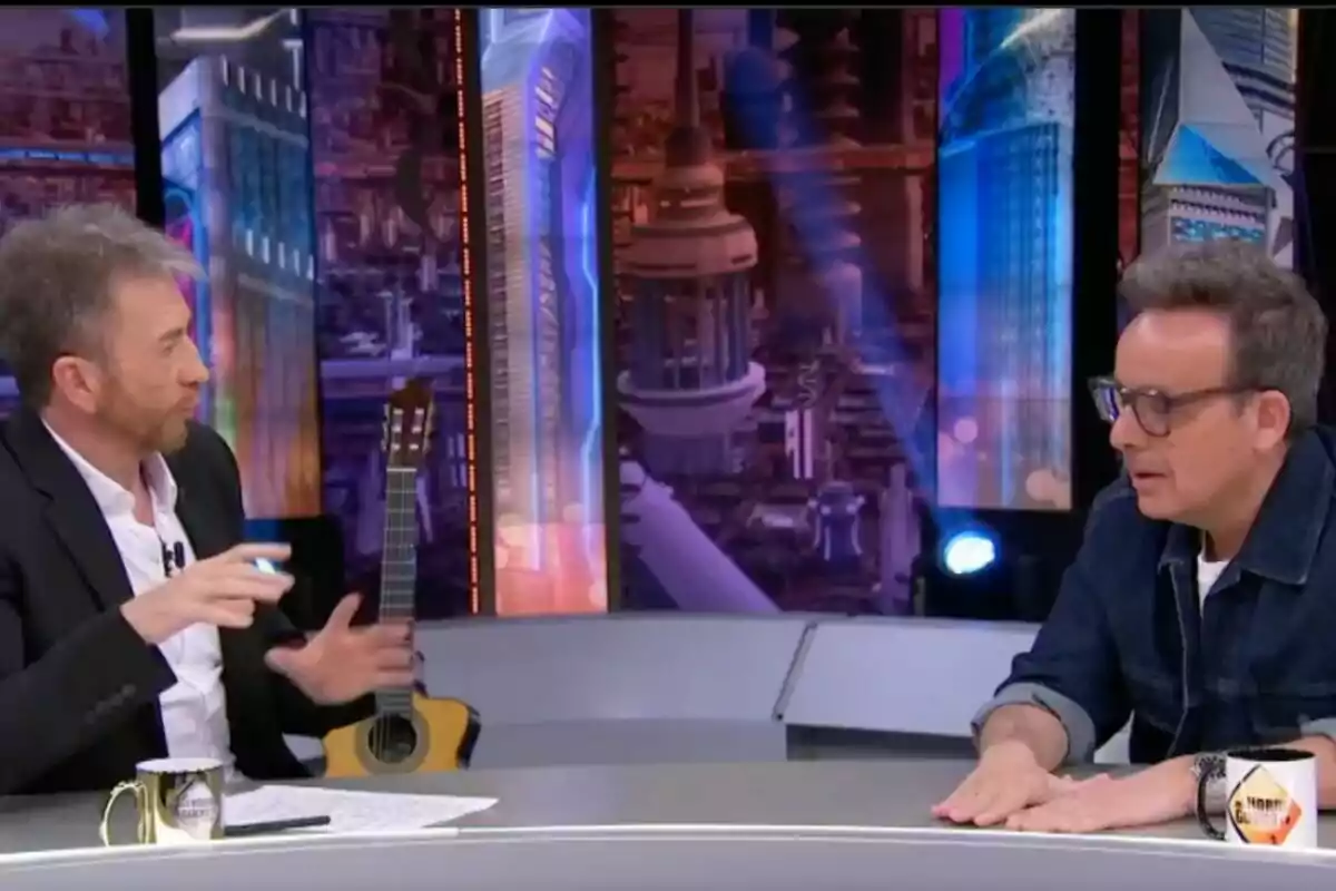 Pablo Motos i Àngel Llàcer conversen en un plató de televisió amb una guitarra al fons i una decoració futurista a 'El Hormiguero'.
