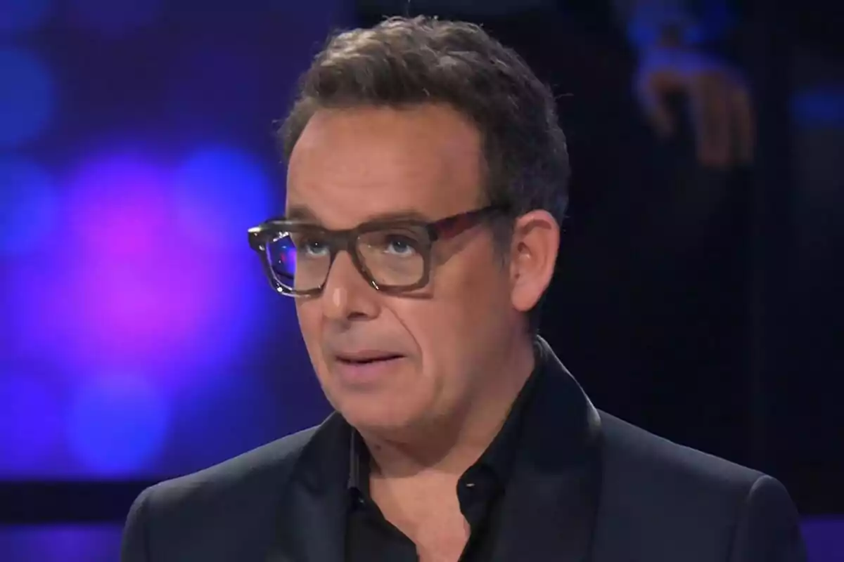 Àngel Llàcer con gafas y cabello corto en un entorno con luces de colores de Tu Cara Me Suena.