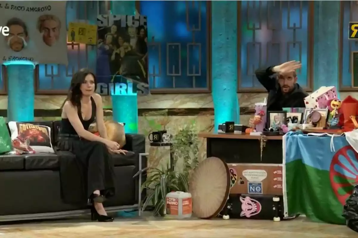 En la imagen se observa un set de televisión con dos personas, Anna Castillo sentada en un sofá y David Broncano detrás de un escritorio, rodeados de decoraciones coloridas y objetos variados en 'La Revuelta'. En la imagen se observa un set de televisión con dos personas, Anna Castillo sentada en un sofá y David Broncano detrás de un escritorio, rodeados de decoraciones coloridas y objetos variados en 'La Revuelta'.