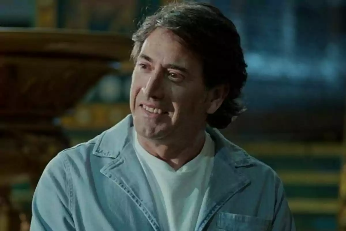 Antonio Garrido con cabello oscuro y chaqueta clara sonríe mientras mira hacia un lado en un entorno interior en Pasión y Gloria.
