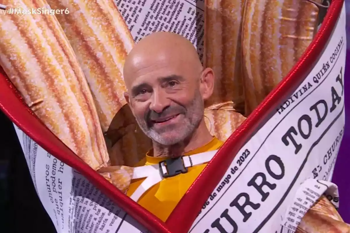 Antonio Lobato calvo sonríe mientras lleva un disfraz de churro envuelto en papel de periódico en Mask Singer. Antonio Lobato calvo sonríe mientras lleva un disfraz de churro envuelto en papel de periódico en Mask Singer.