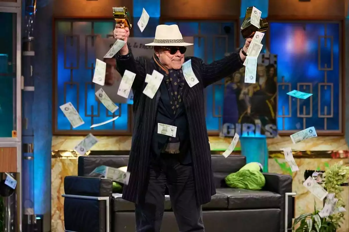 Antonio Resines con sombrero y gafas de sol sostiene dos pistolas de juguete doradas mientras billetes falsos vuelan a su alrededor en La Revuelta. Antonio Resines con sombrero y gafas de sol sostiene dos pistolas de juguete doradas mientras billetes falsos vuelan a su alrededor en La Revuelta.