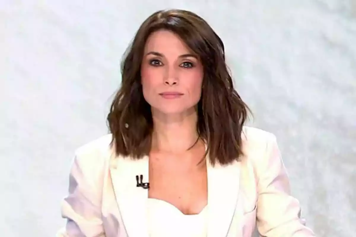 Arancha Morales amb cabell castany i ondulat portant un vestit blanc davant d'un fons clar a Informatius Telecinco.