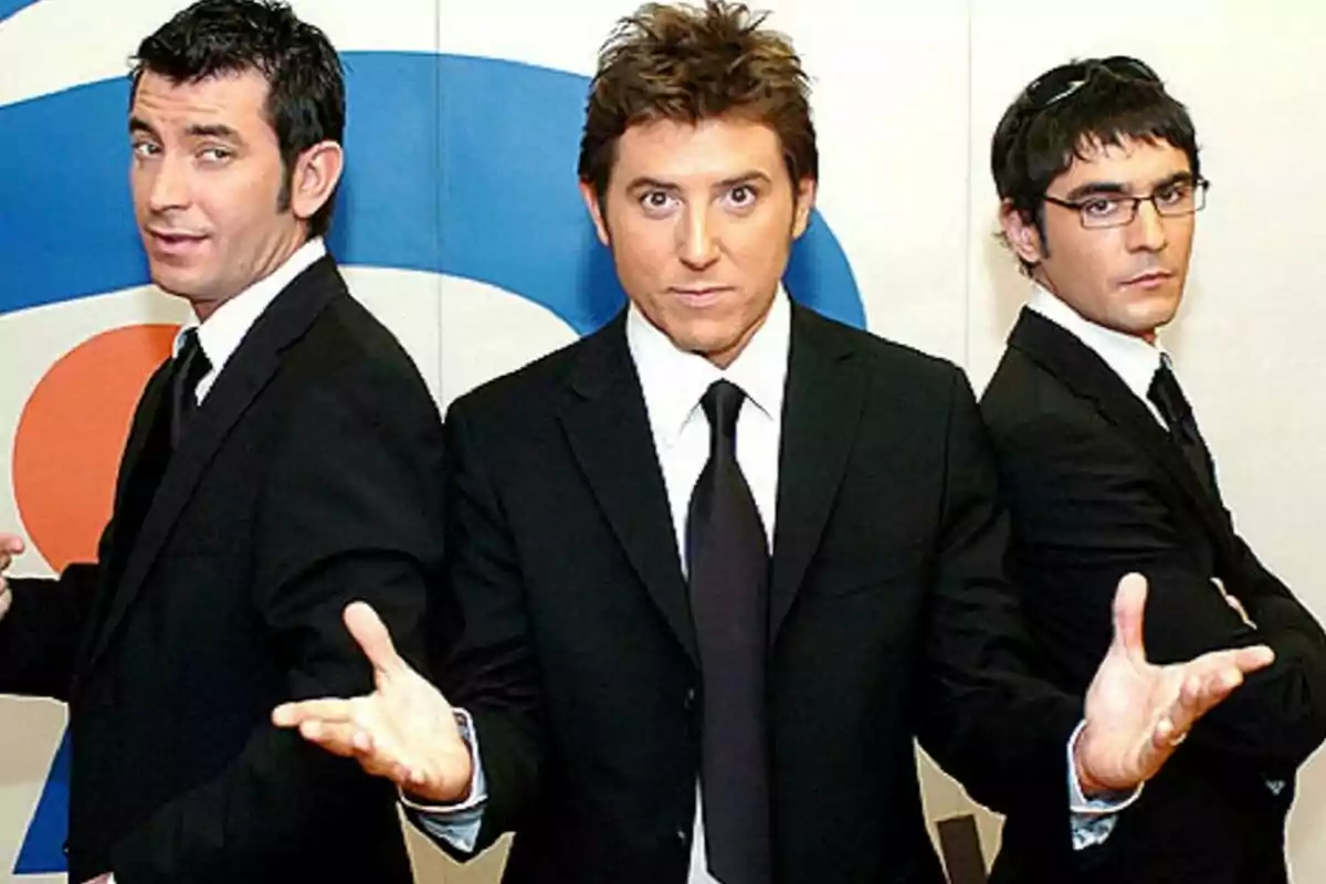 Arturo Valls, Manel Fuentes y Juanra Bonet vestidos con trajes oscuros posan frente a un fondo con un diseño colorido en Caiga quien caiga. Arturo Valls, Manel Fuentes y Juanra Bonet vestidos con trajes oscuros posan frente a un fondo con un diseño colorido en Caiga quien caiga.