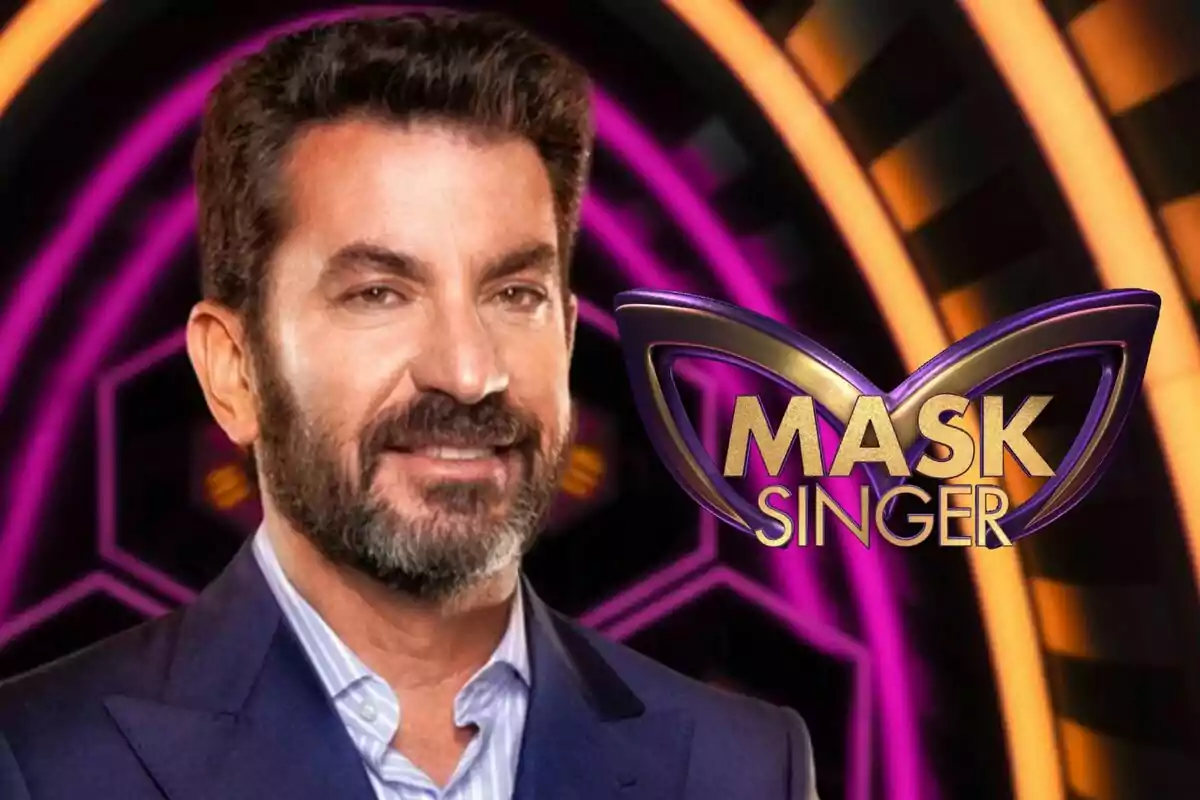 Arturo Valls amb barba i vestit fosc apareix davant d'un fons acolorit amb el logotip de "Mask Singer".