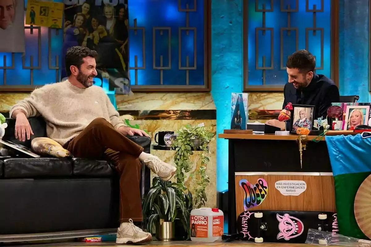 Arturo Valls y David Broncano conversan y ríen en La Revuelta decorado con plantas, carteles y objetos variados. Arturo Valls y David Broncano conversan y ríen en La Revuelta decorado con plantas, carteles y objetos variados.
