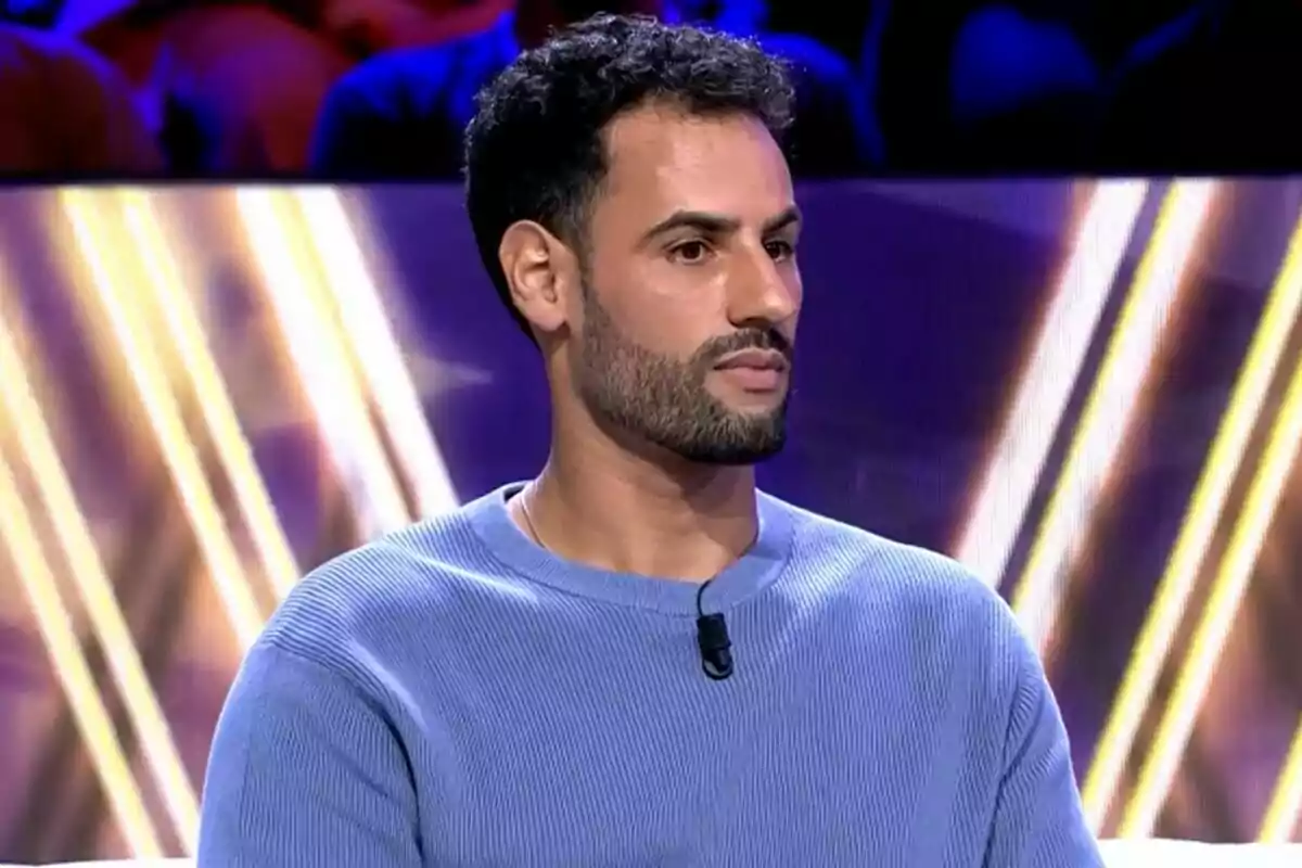 Asraf Beno con barba y cabello oscuro lleva un suéter azul y está sentado en el plató de De Viernes. Asraf Beno con barba y cabello oscuro lleva un suéter azul y está sentado en el plató de De Viernes.