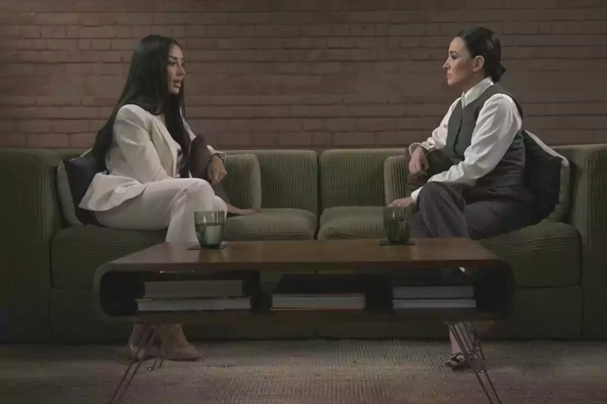 Aurah Ruiz y Cruz Sánchez de Lara sentadas en un sofá verde, frente a frente, en una conversación en un ambiente interior con una mesa de centro de madera y vasos sobre ella en Madres: desde el corazón. Aurah Ruiz y Cruz Sánchez de Lara sentadas en un sofá verde, frente a frente, en una conversación en un ambiente interior con una mesa de centro de madera y vasos sobre ella en Madres: desde el corazón.