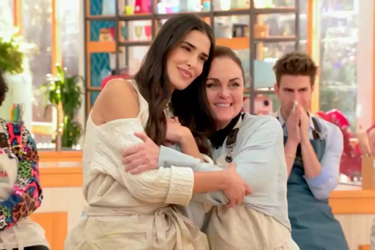 Lidia Torrent i Carmen Morales abraçant-se amb somriures en un ambient de cuina, mentre una altra persona al fons observa amb les mans juntes a 'Bake off: Famosos al forn'.