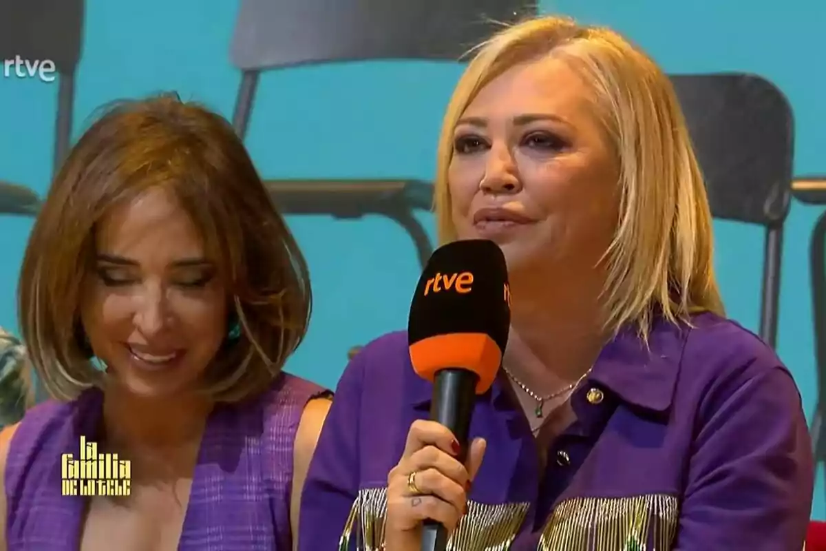 María Patiño i Belén Esteban estan assegudes en un escenari, una d'elles sosté un micròfon amb el logotip de RTVE, ambdues semblen estar participant en un programa anomenat 