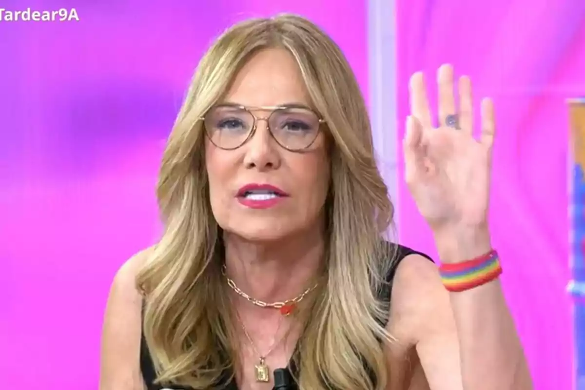 Belén Rodríguez amb ulleres i cabell ros està aixecant la mà, portant una polsera de colors i un fons rosa a Tardear. Belén Rodríguez amb ulleres i cabell ros està aixecant la mà, portant una polsera de colors i un fons rosa a Tardear.