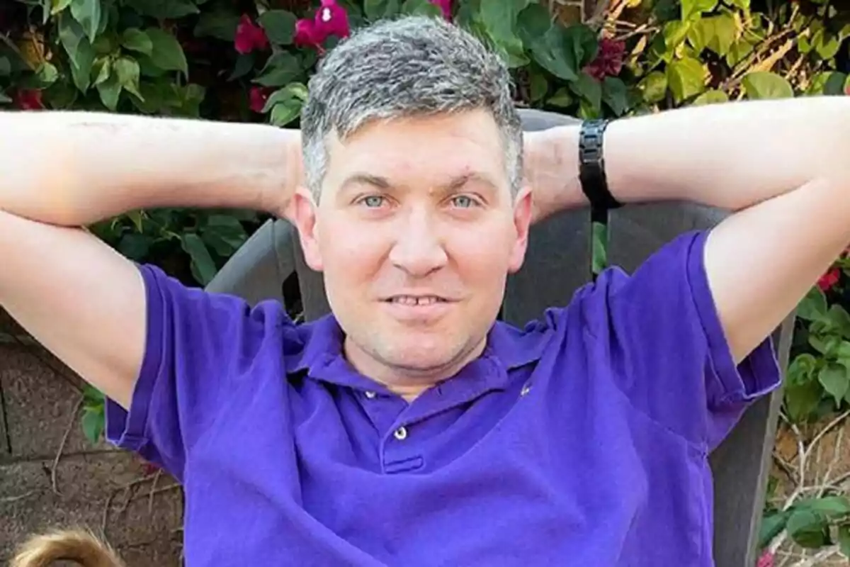 Fotografía de Benji Gregory con camisa morada relajándose en una silla al aire libre con plantas de fondo. Fotografía de Benji Gregory con camisa morada relajándose en una silla al aire libre con plantas de fondo.