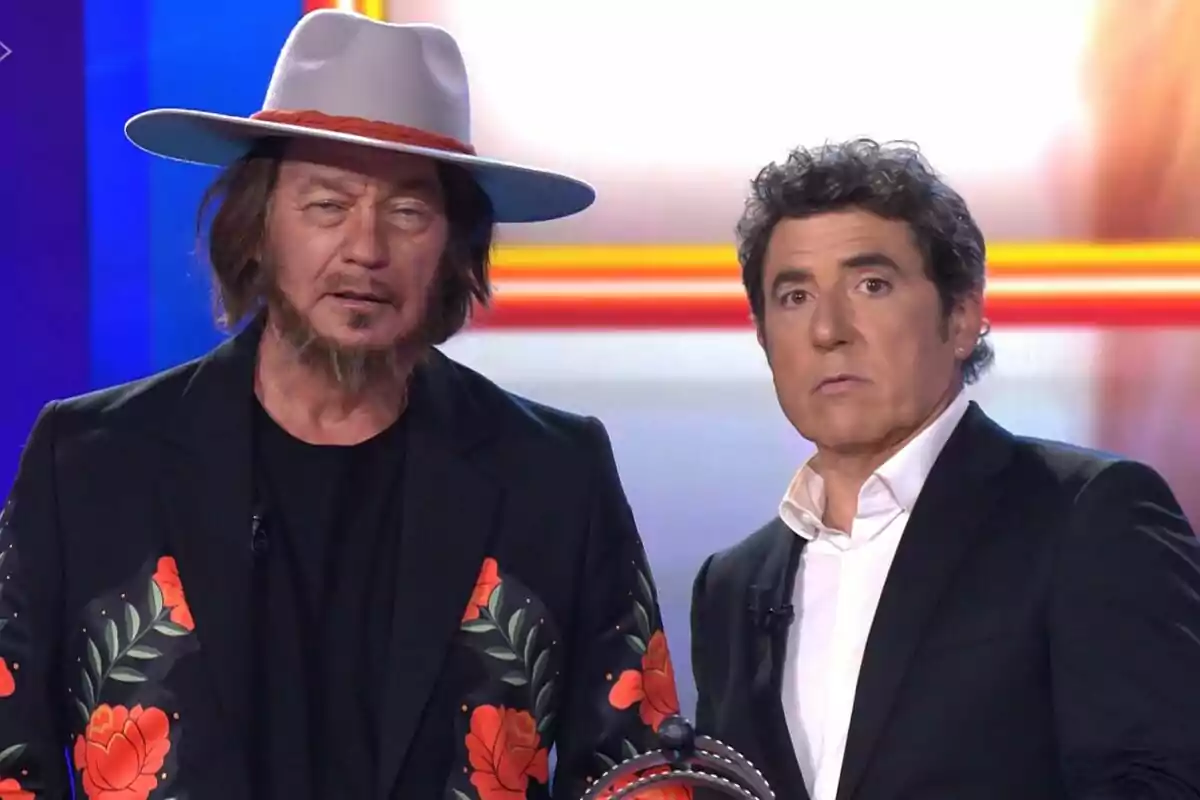 Bertín Osborne y Manel Fuentes en un set de Tu Cara Me Suena uno lleva sombrero gris y chaqueta con flores rojas y el otro viste traje negro con camisa blanca Bertín Osborne y Manel Fuentes en un set de Tu Cara Me Suena uno lleva sombrero gris y chaqueta con flores rojas y el otro viste traje negro con camisa blanca
