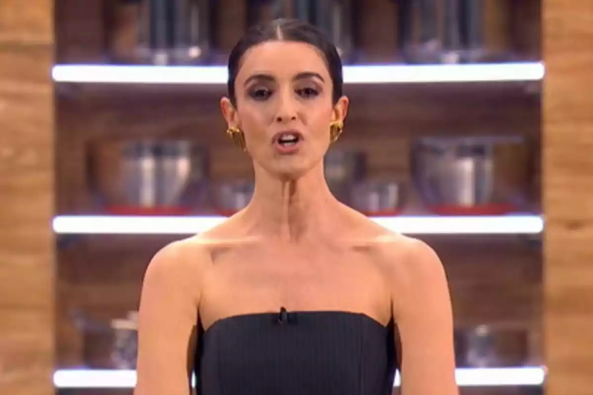 Blanca Romero amb cabell fosc recollit i anells daurats està parlant a Next Level Xef amb prestatges i estris de cuina de fons.